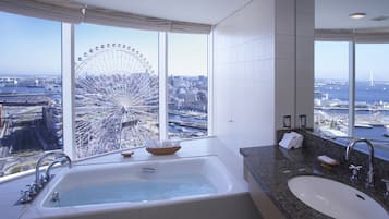Un baño moderno con una bañera grande, un lavamanos y vistas a una noria y al paisaje urbano.