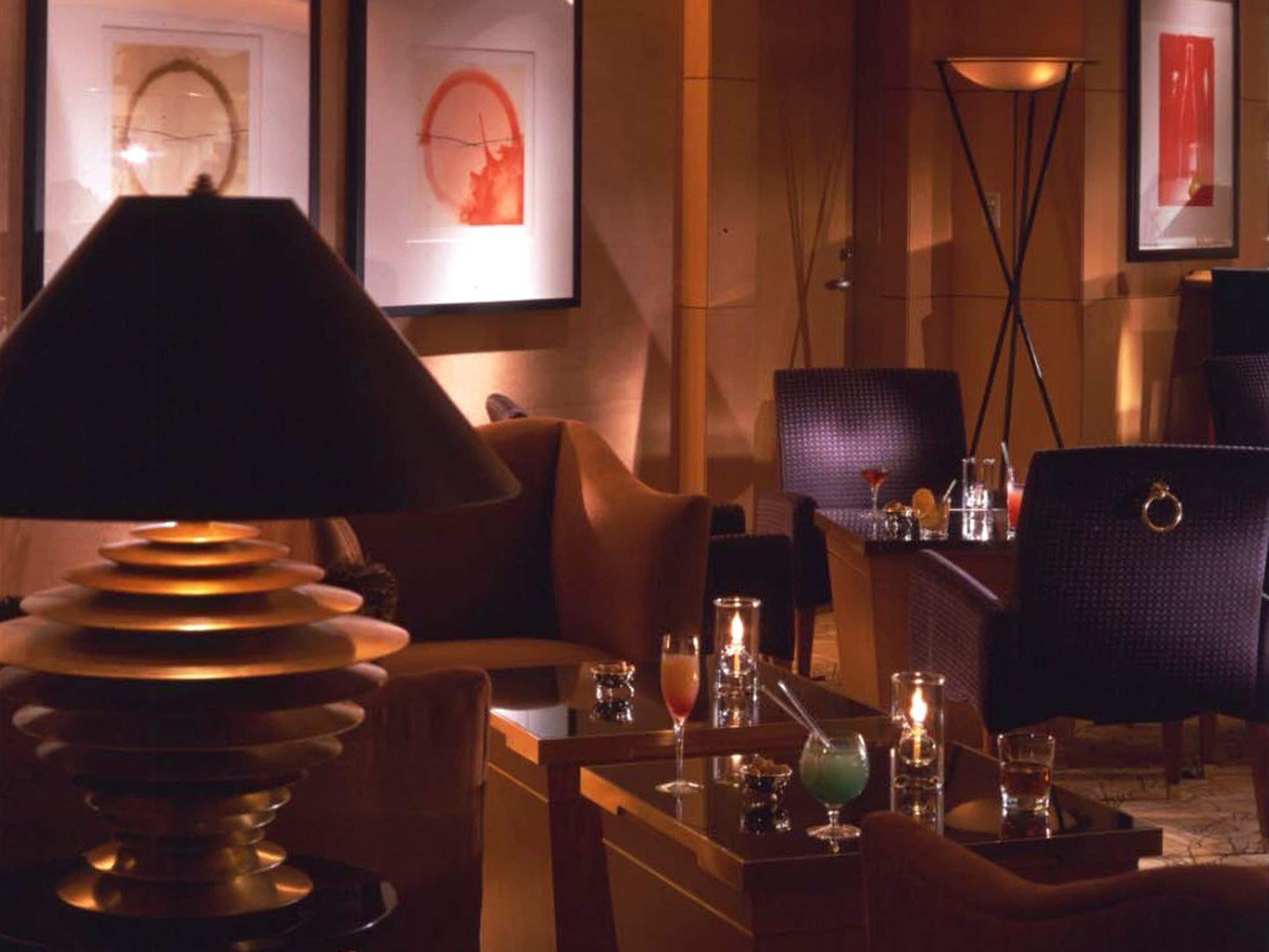 A dimly lit lounge area with a table set for two, featuring a lamp, candles, and a glass of water.