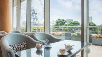 Une chambre moderne avec une table en verre, deux chaises et une vue sur une grande roue et le paysage urbain.
