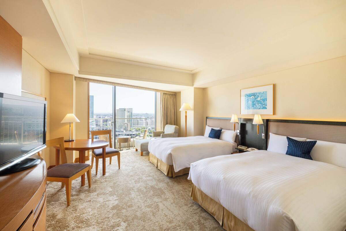 Habitación de hotel con dos camas, un escritorio, una televisión y vista a la ciudad.