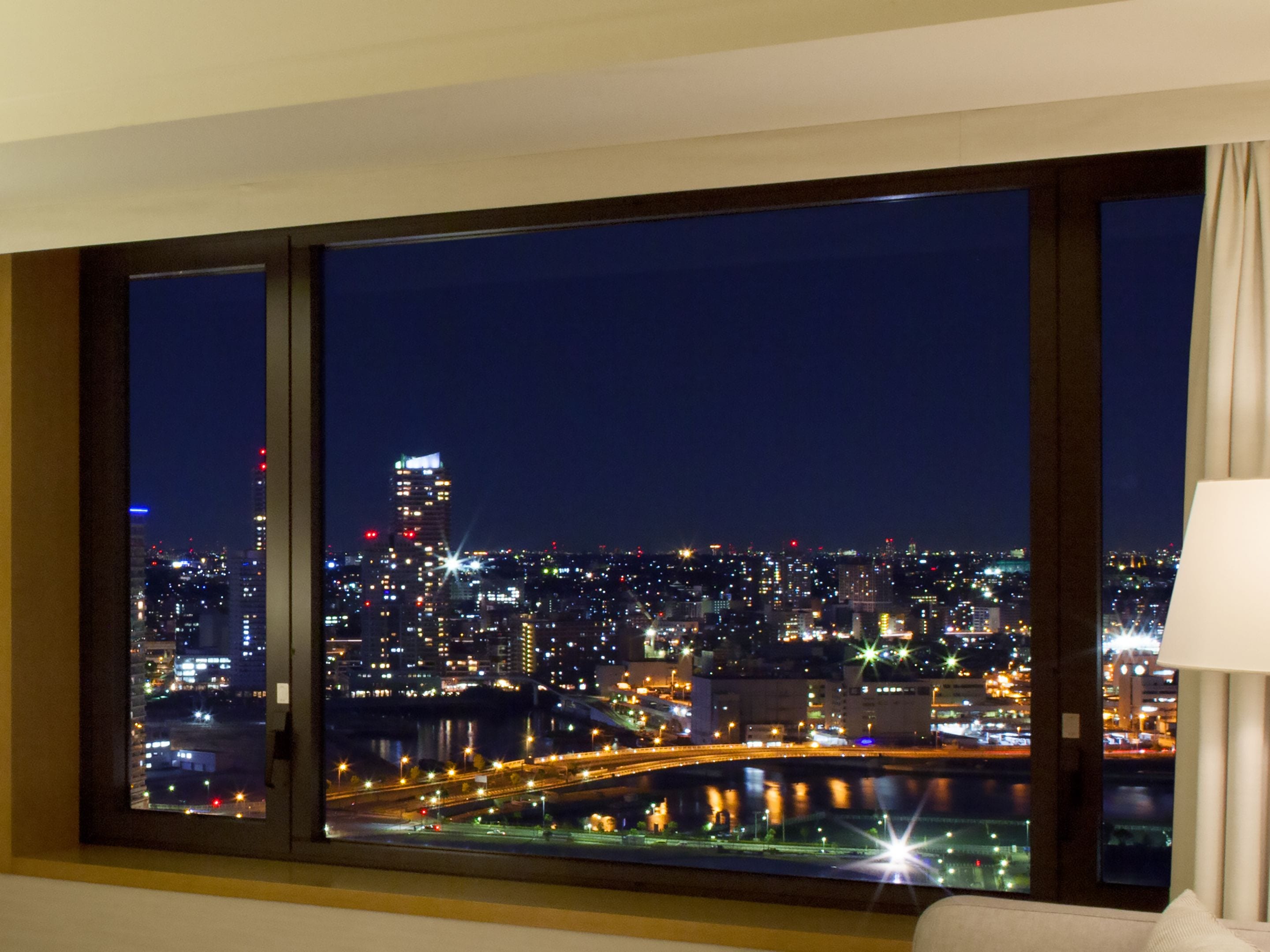 A large window with a cityscape view at night, including illuminated buildings and a bridge.