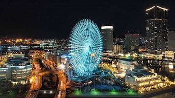 Una noria grande con estructura iluminada en azul, rodeada de edificios modernos y un muelle.