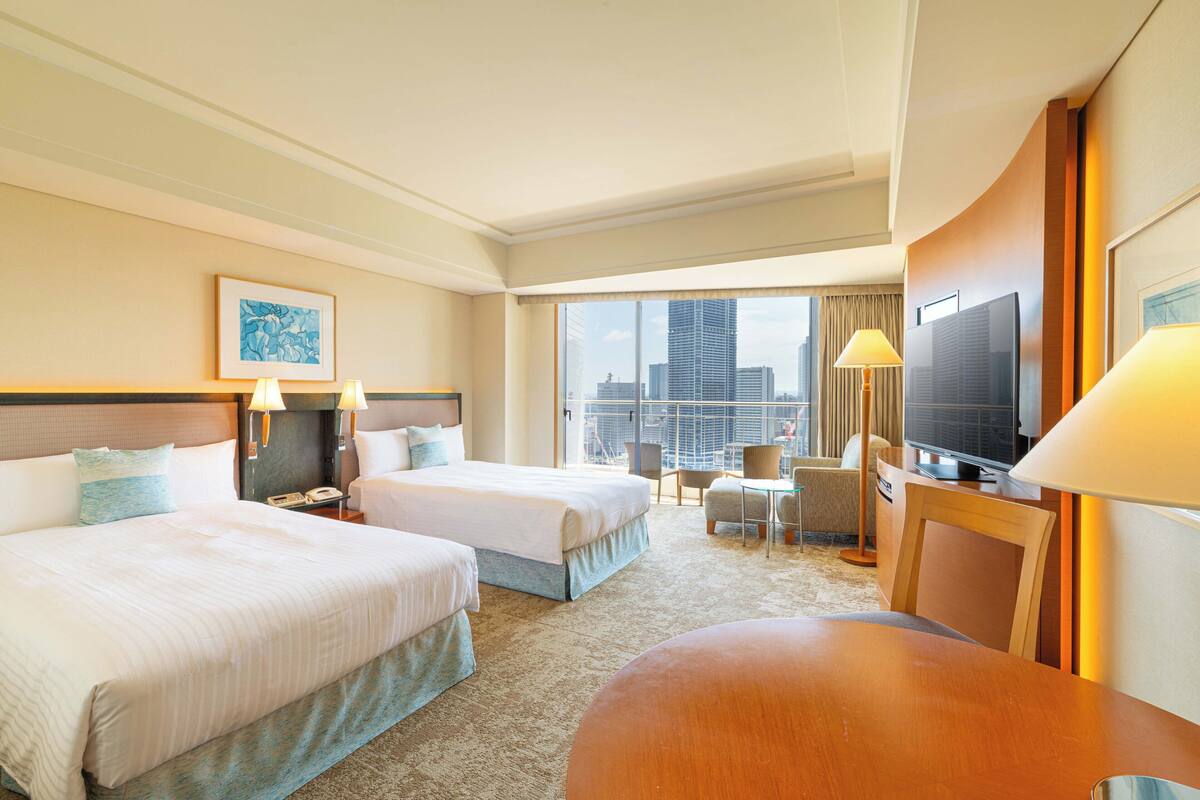 Habitación de hotel con dos camas, televisión, escritorio y vista a la ciudad.