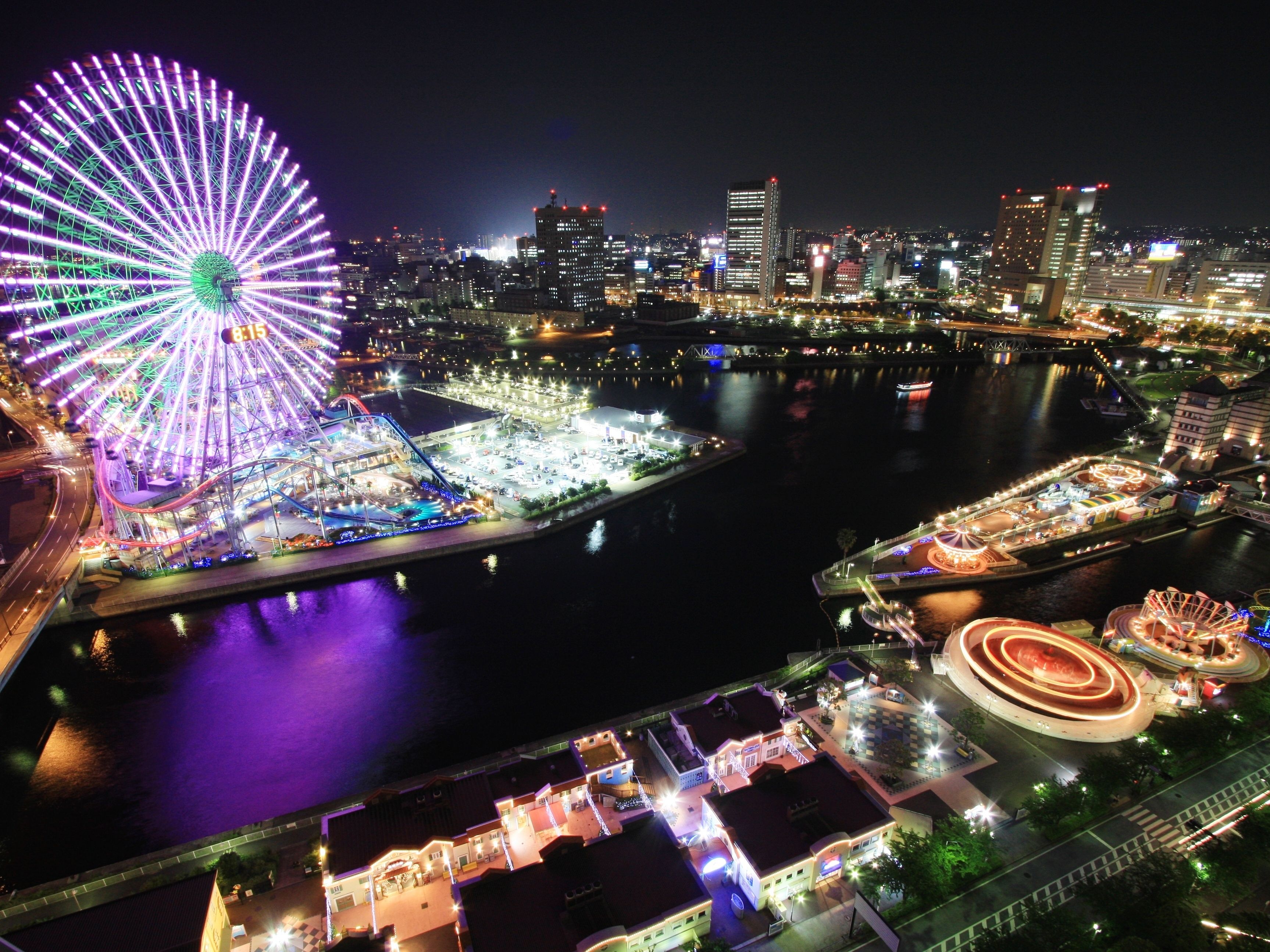 A nighttime cityscape with a prominent Ferris wheel and a waterfront area.
