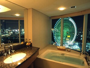Un baño con lavabo, bañera, espejo y vistas a un paisaje urbano de noche.