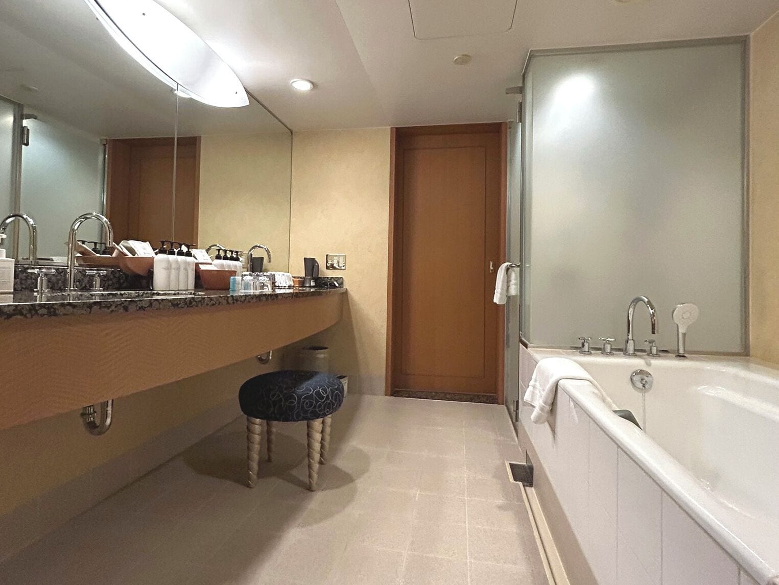 A hotel bathroom with a large mirror, a sink with toiletries, a toilet, and a bathtub.