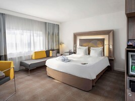 Una habitación de hotel con una cama grande, un sofá, un escritorio y un miniibar.