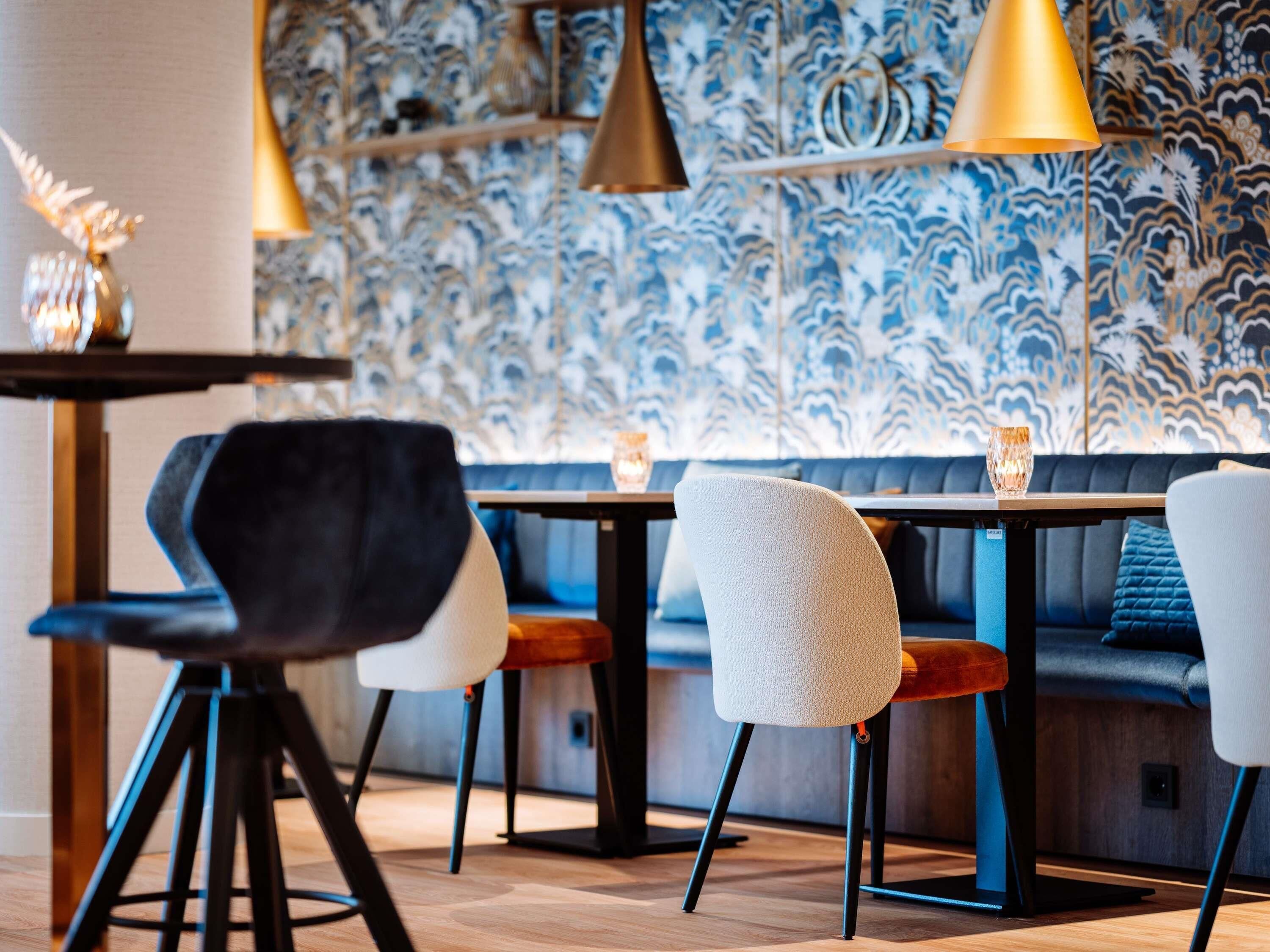 A modern dining area with a patterned wall, black and white chairs, and pendant lighting.