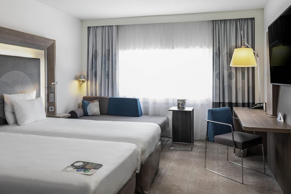 Habitación de hotel con dos camas, un escritorio, una silla, una lámpara y un televisor.