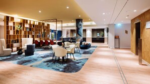 Um lobby moderno com área de estar central, uma grande estante e um balcão de recepção de madeira.