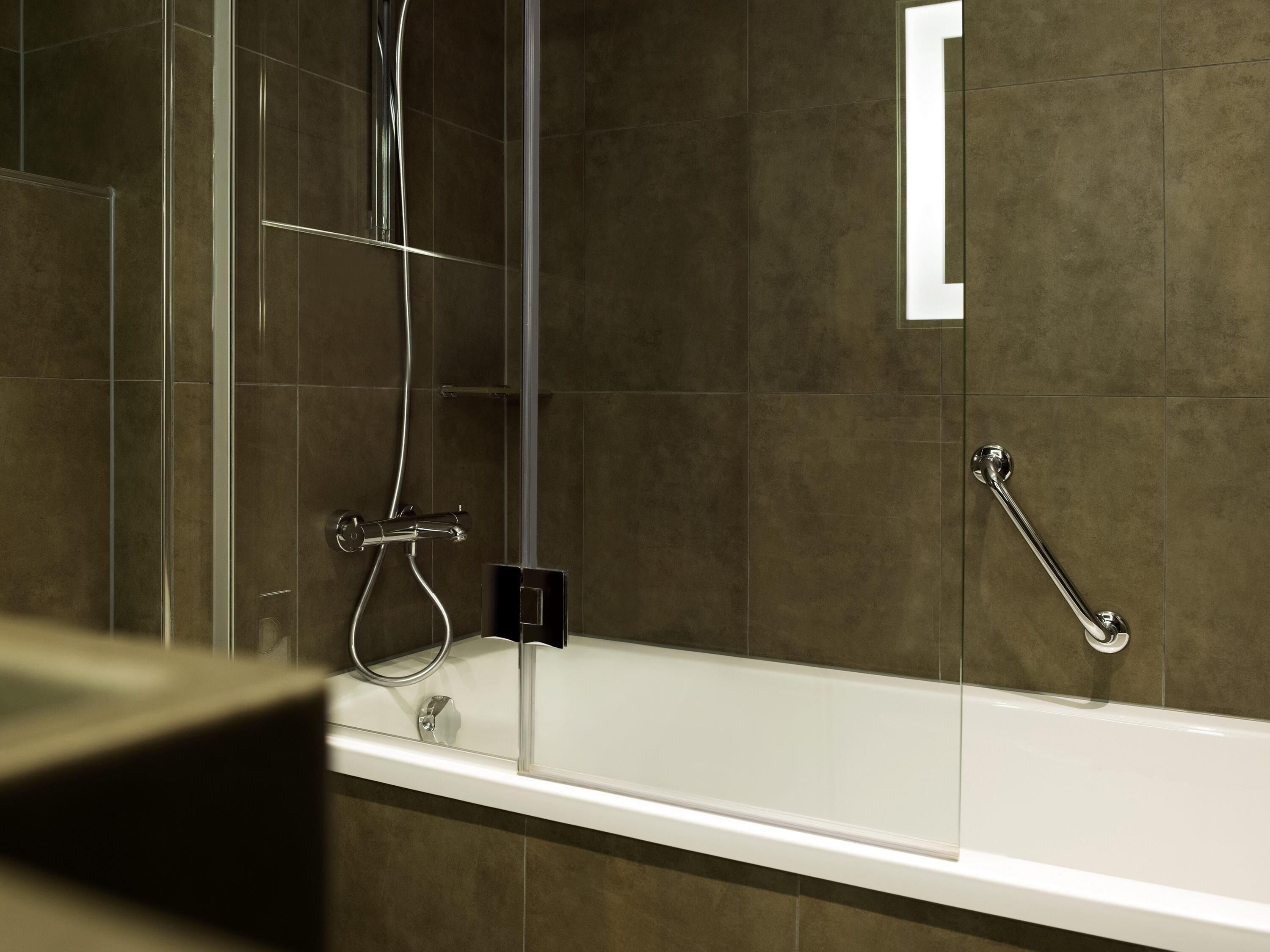 Een moderne badkamer met een douche met glazen wand, een witte badkuip en een handgreep.