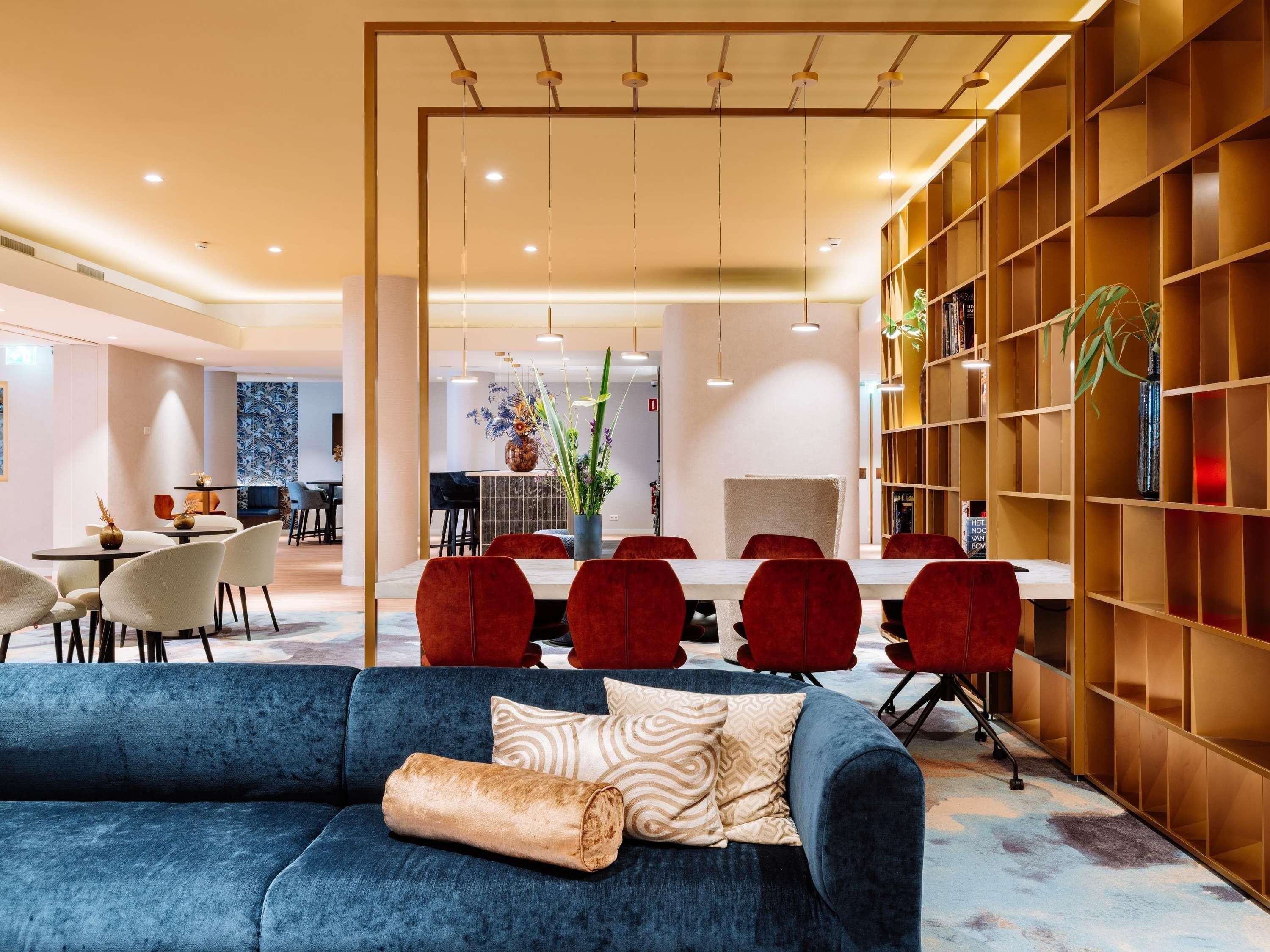 Una sala de estar moderna con un sofá azul, sillas rojas, una zona de comedor y una estantería.