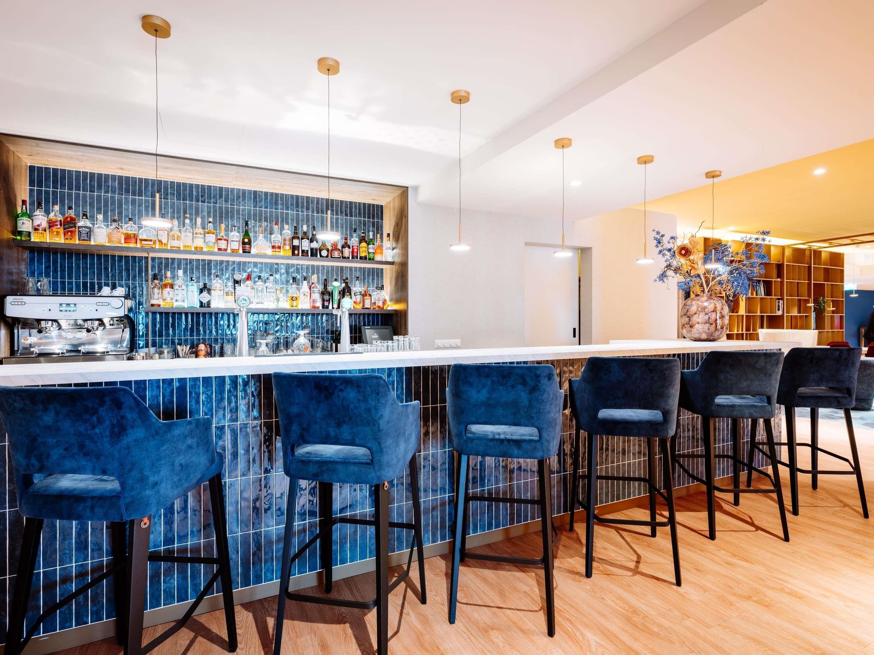 Uma área de bar com balcão, vários bancos, uma máquina de café e uma variedade de garrafas.