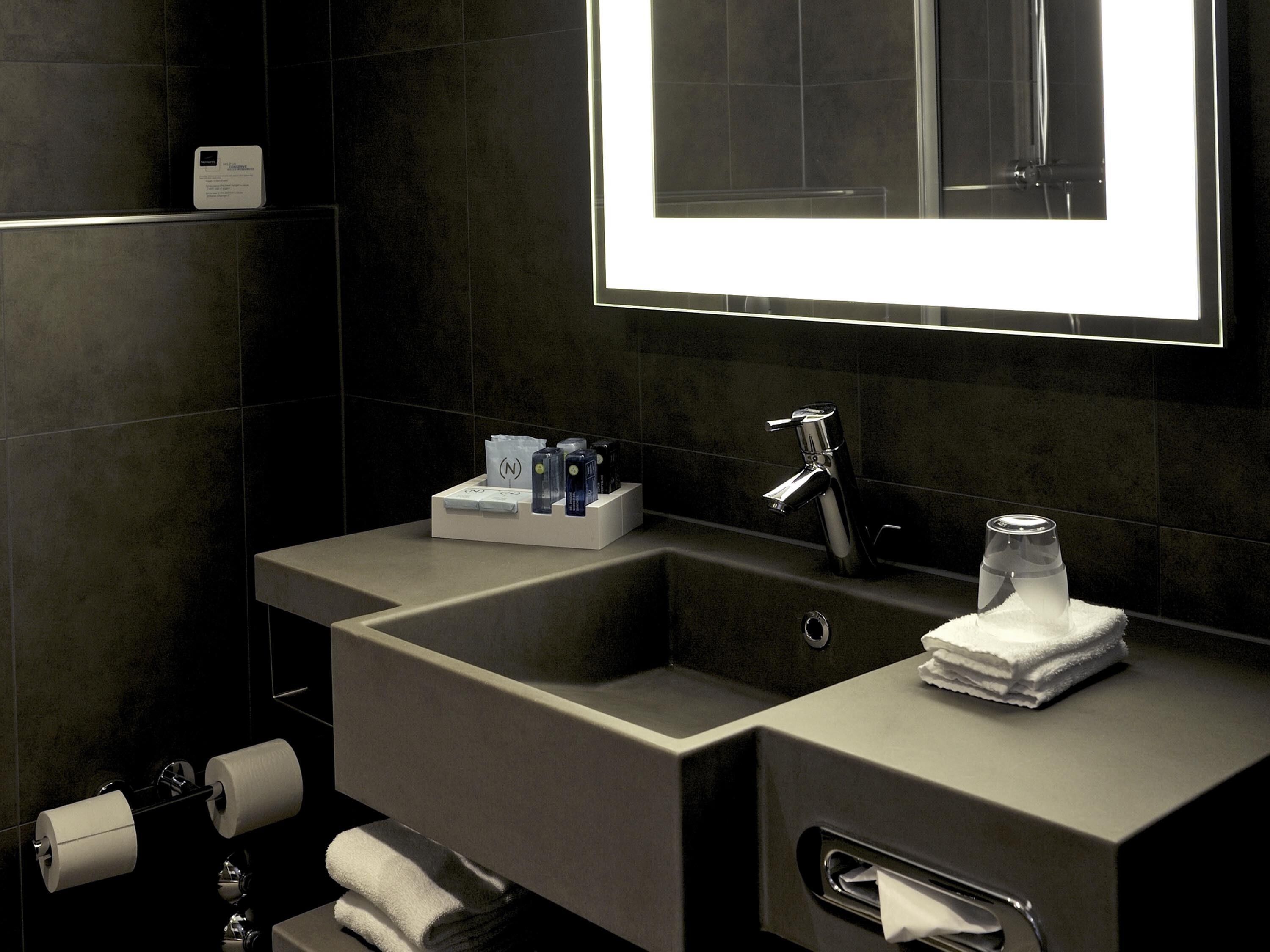 A modern bathroom with a large mirror, two sinks, a towel rack, and a toilet paper holder.