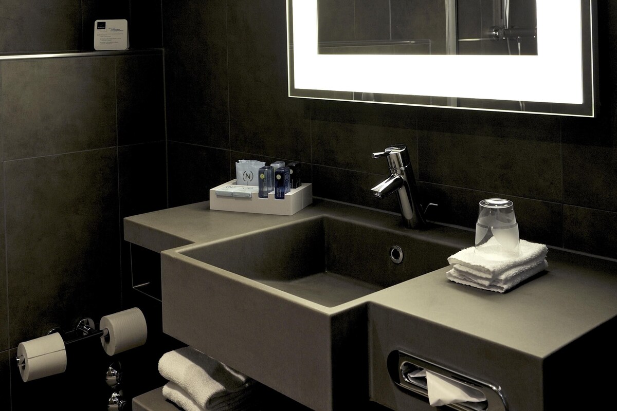A modern bathroom with a large mirror, two sinks, a towel rack, and a toilet paper holder.