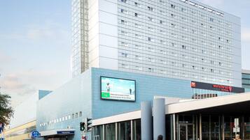 Een Novotel hotel met een groot reclamebord, een fietsenstalling en een voetgangersoversteekplaats.