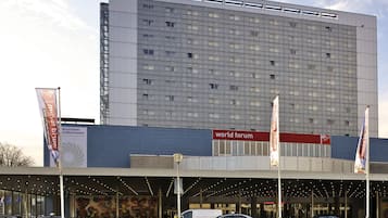 Un hotel con una fachada amplia y moderna, un cartel llamativo de 'Novotel' y un cartel de 'World Forum' que indica una zona de conferencias.
