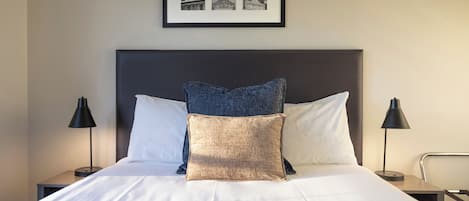 A neatly made bed with a headboard, two bedside lamps, and a framed picture above the bed.