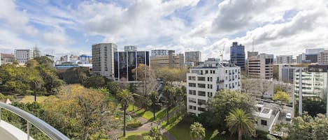 A high-rise building with a view of a cityscape, including other buildings and a park area with palm trees.