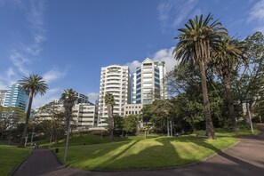 A park with a walking path, palm trees, and modern buildings in the background. - Quest Auckland (Auckland)