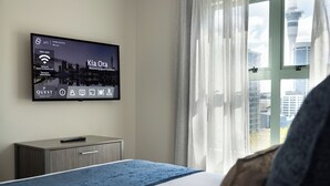 Habitación de hotel con una cama, un televisor mostrando un paisaje urbano, un escritorio y una ventana con vistas a una torre.