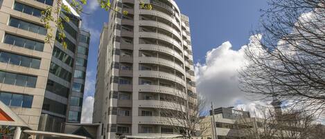 A multi-story building with a curved facade, a prominent entrance labeled "Quest," and a clear sky with clouds.