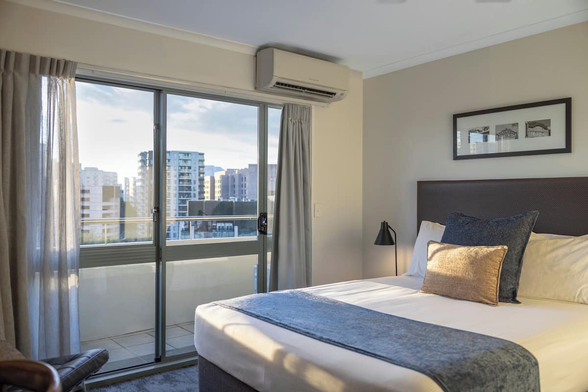 A hotel room with a large bed, a view of the city through a sliding glass door, and a framed picture on the wall.