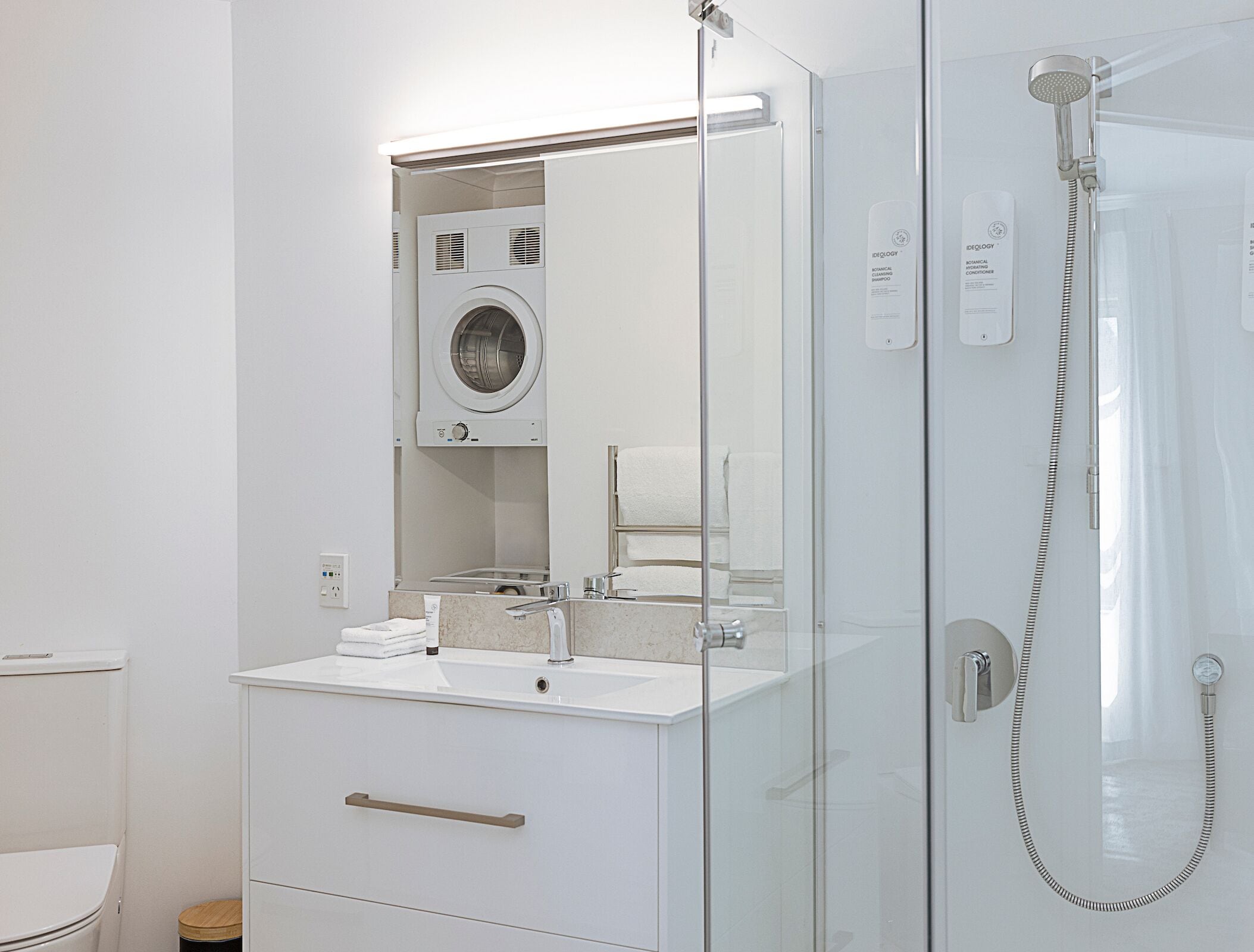 A modern bathroom with a glass-enclosed shower, a built-in washing machine, and a vanity with a sink and mirror.