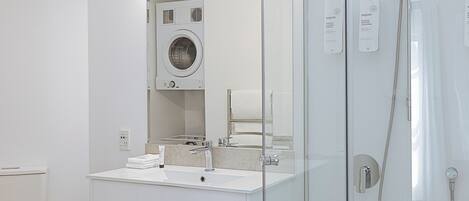 A modern bathroom with a glass-enclosed shower, a built-in washing machine, and a vanity with a sink and mirror.