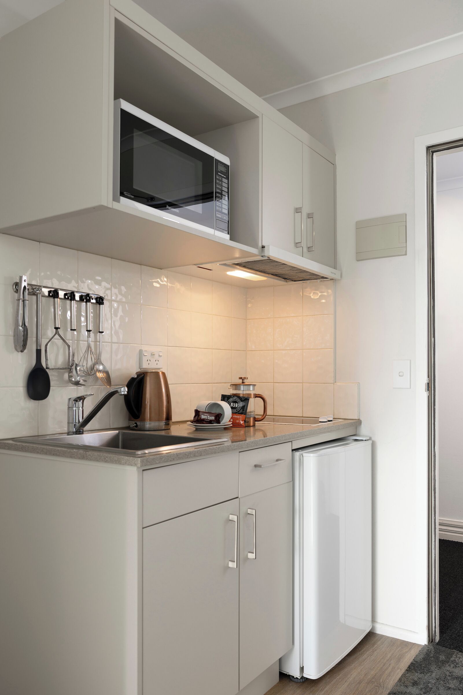 A compact kitchen with white cabinets, a stainless steel sink, a microwave, and a coffee maker.