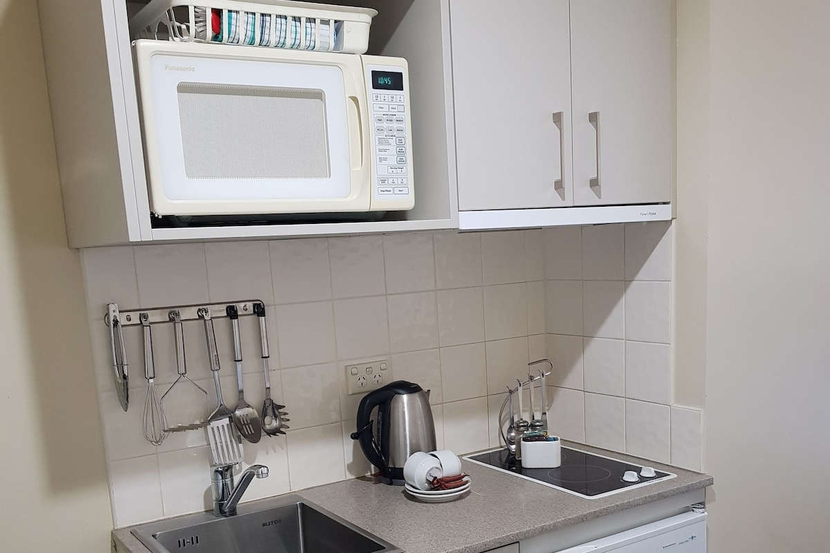 Una cocina compacta con microondas, hervidor, pileta y utensilios.