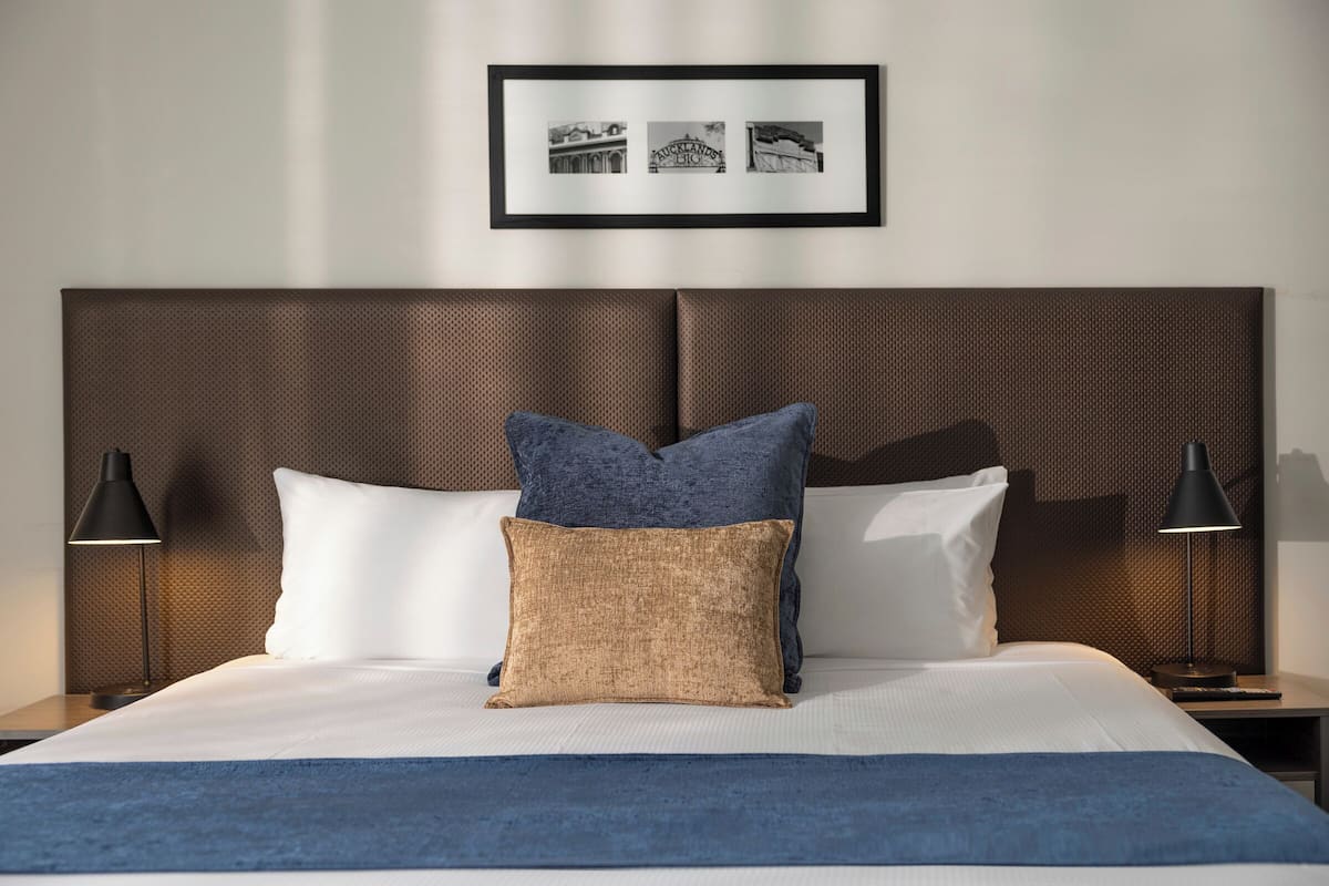 A neatly made bed with a blue throw blanket, two pillows, and a framed picture above it.
