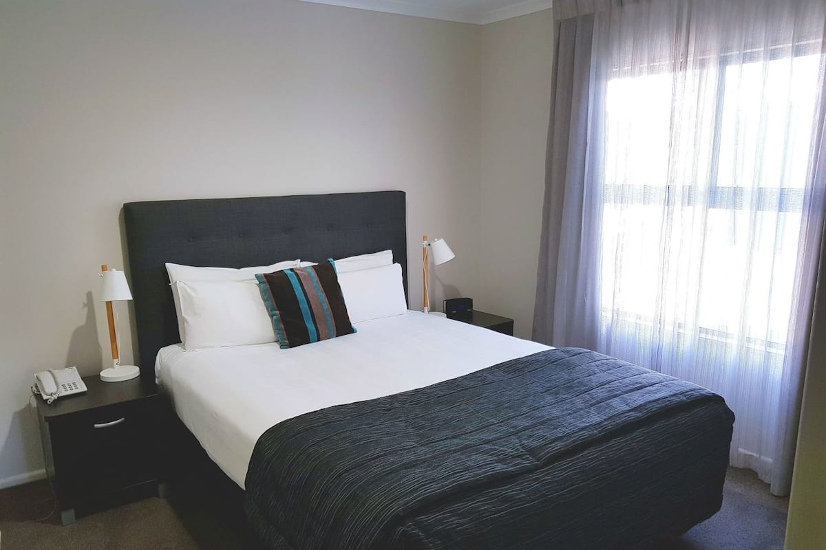 A hotel room with a bed, bedside lamps, a phone, and a window with curtains.