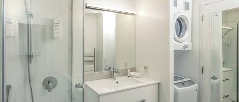 Une salle de bain moderne avec une douche à parois de verre, un lavabo blanc avec un miroir au-dessus, et un lave-linge encastré.