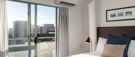 Une chambre d’hôtel avec un grand lit, une vue sur la ville depuis un balcon et un appareil de climatisation.
