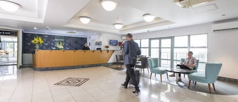 A hotel lobby with a reception desk, seating area, and large windows.