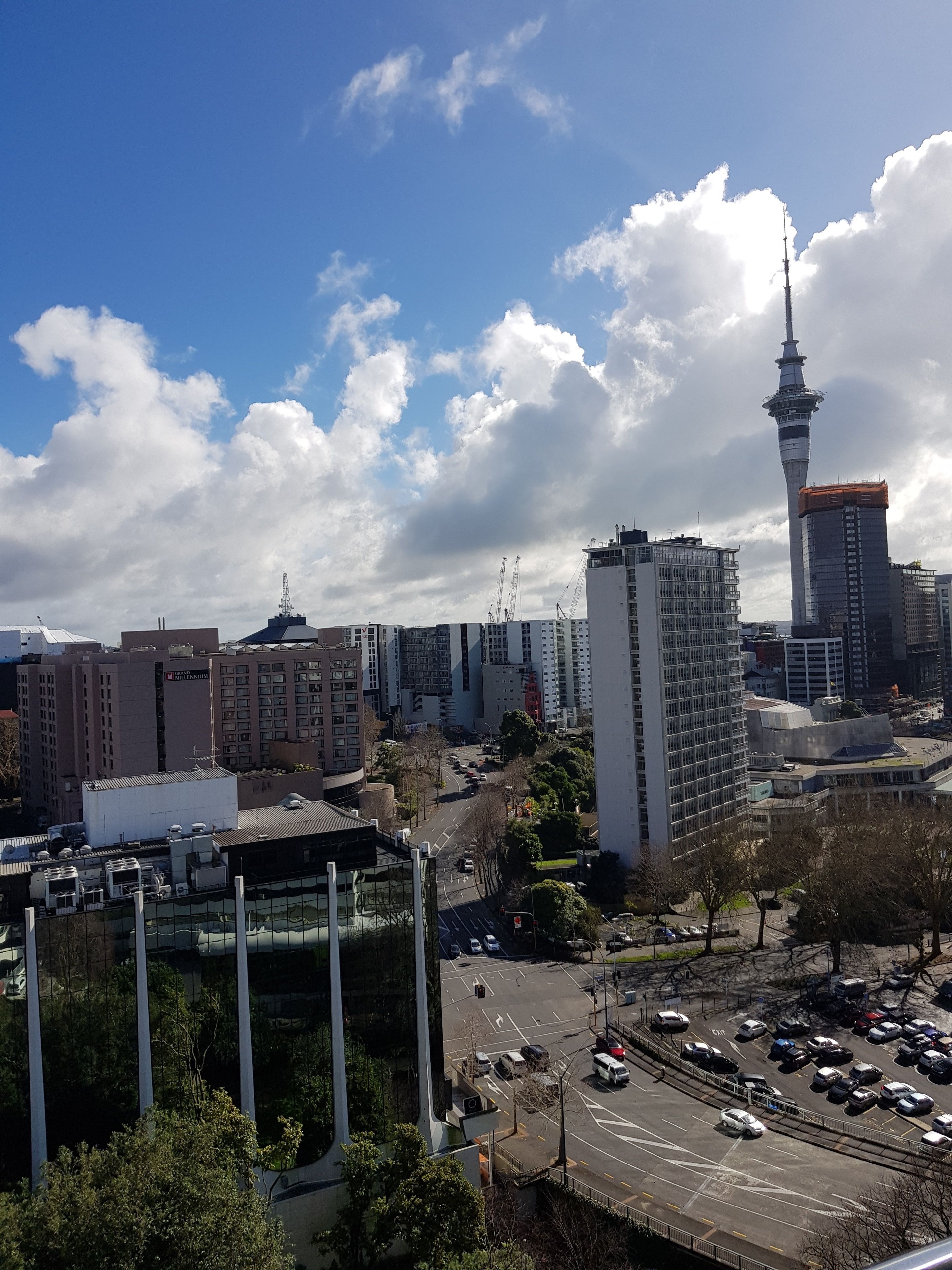A cityscape with a prominent tower, modern buildings, and a parking area.