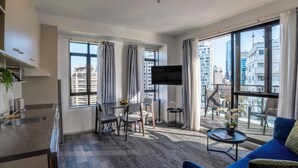 Un apartamento moderno con cocina, comedor y sala de estar. Cuenta con ventanas amplias, un televisor de pantalla plana y un balcón con mobiliario exterior.
