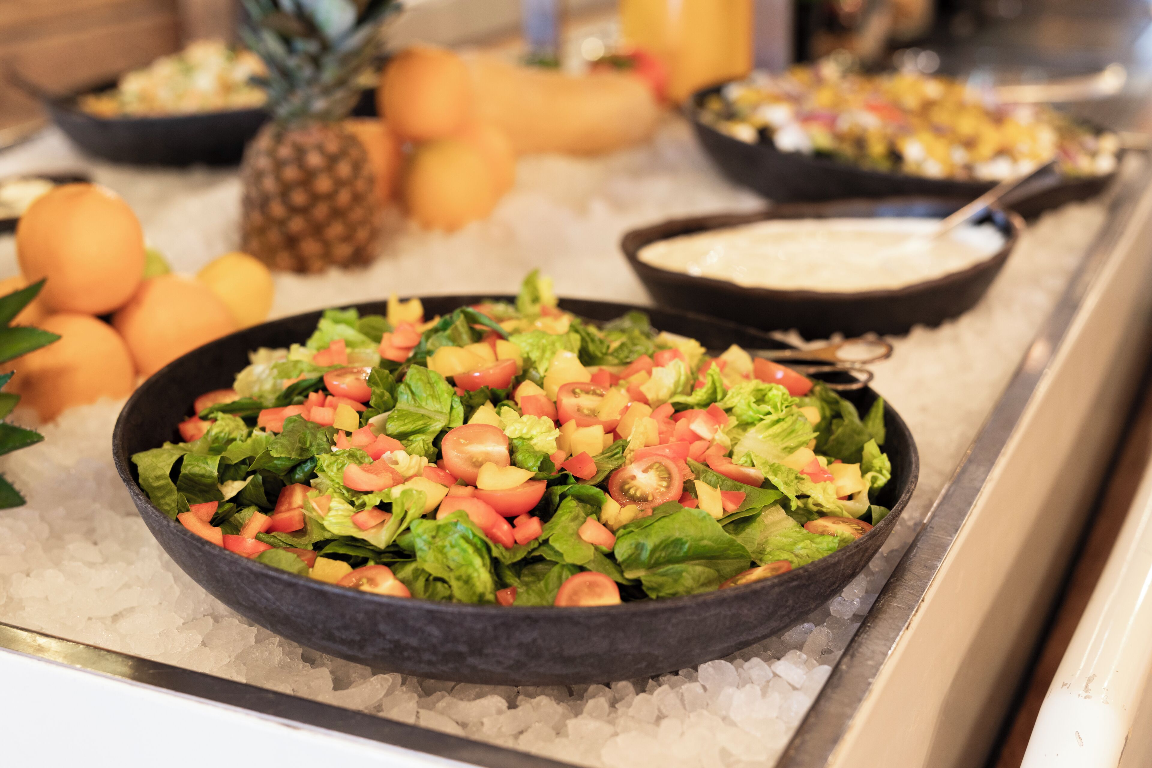 A buffet with a variety of dishes including a salad, fruits, and a creamy soup.