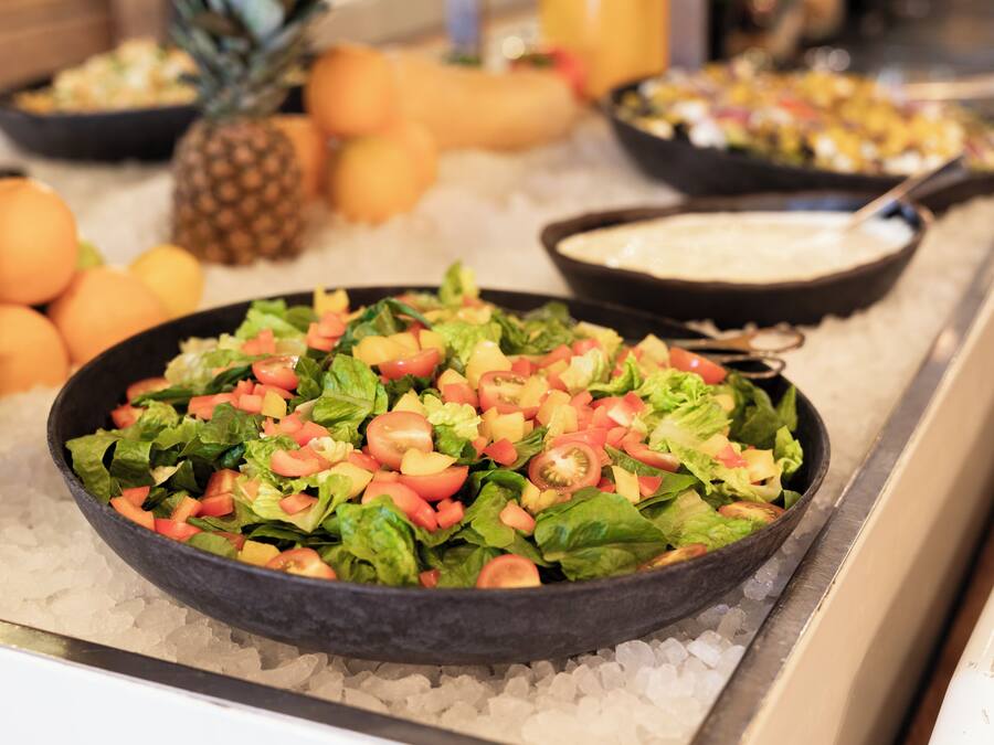A buffet with a variety of dishes including a salad, fruits, and a creamy soup.