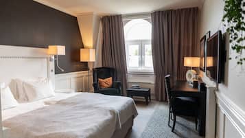 A hotel room with a large bed, a desk with a chair, a TV, and a window with curtains.