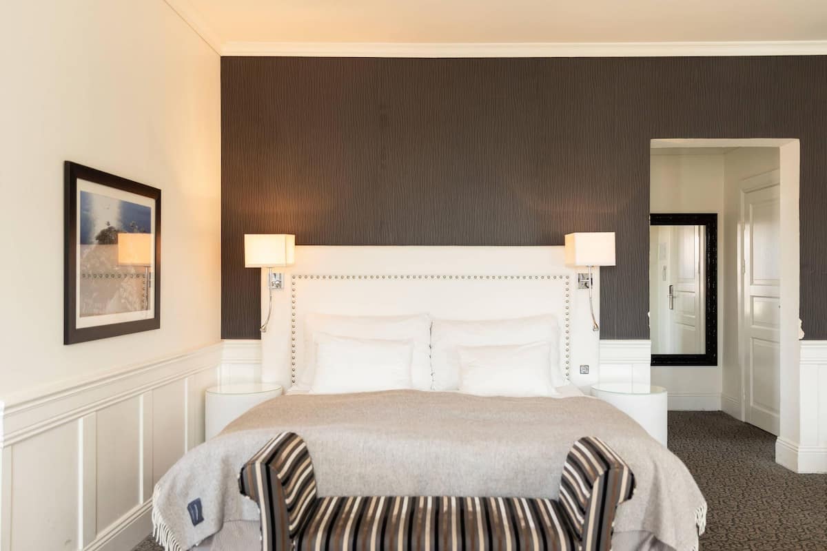 A hotel room with a large bed, two bedside lamps, a framed picture on the wall, and a mirror above the door.