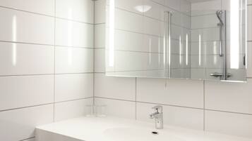 Een moderne badkamer met witte tegels, een grote spiegel, een wastafel en een douche.