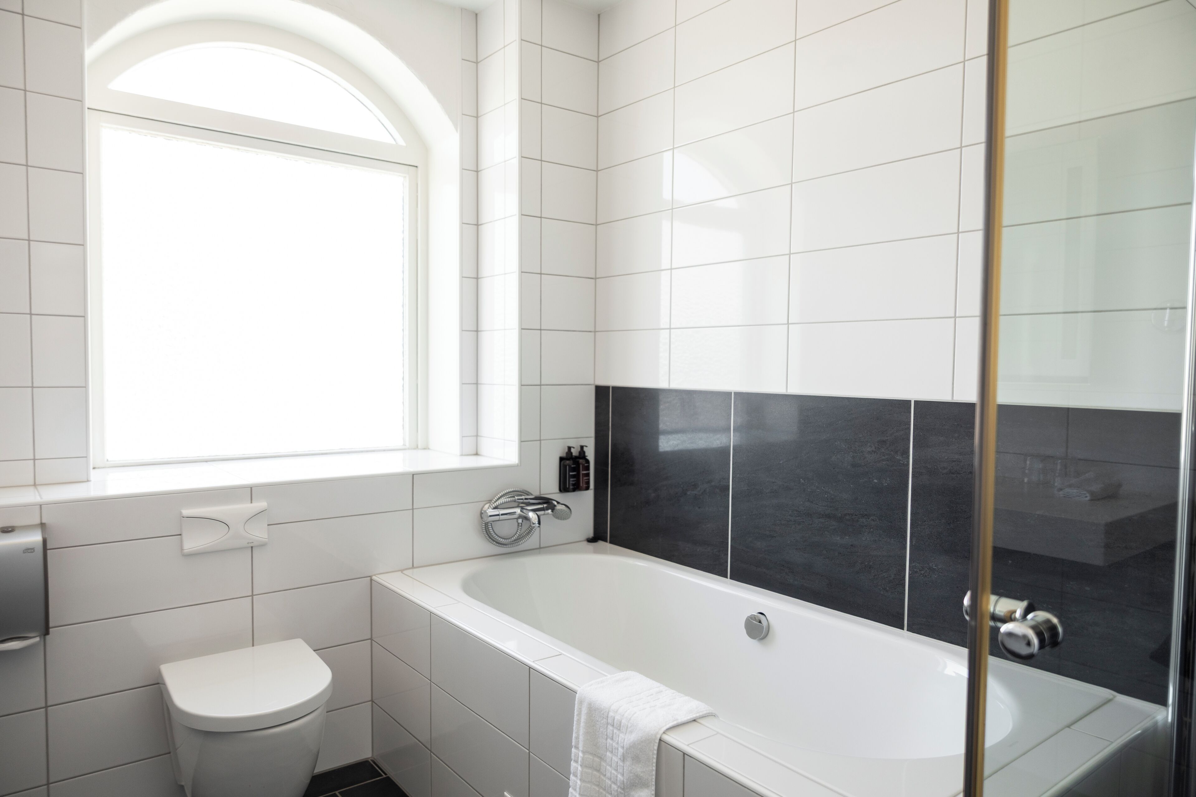 A modern bathroom with a white toilet, a bathtub, and a window.