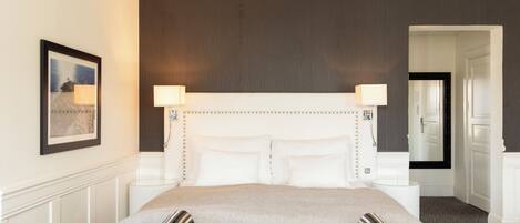 A hotel room with a large bed, two bedside lamps, a framed picture on the wall, and a mirror above the bed.