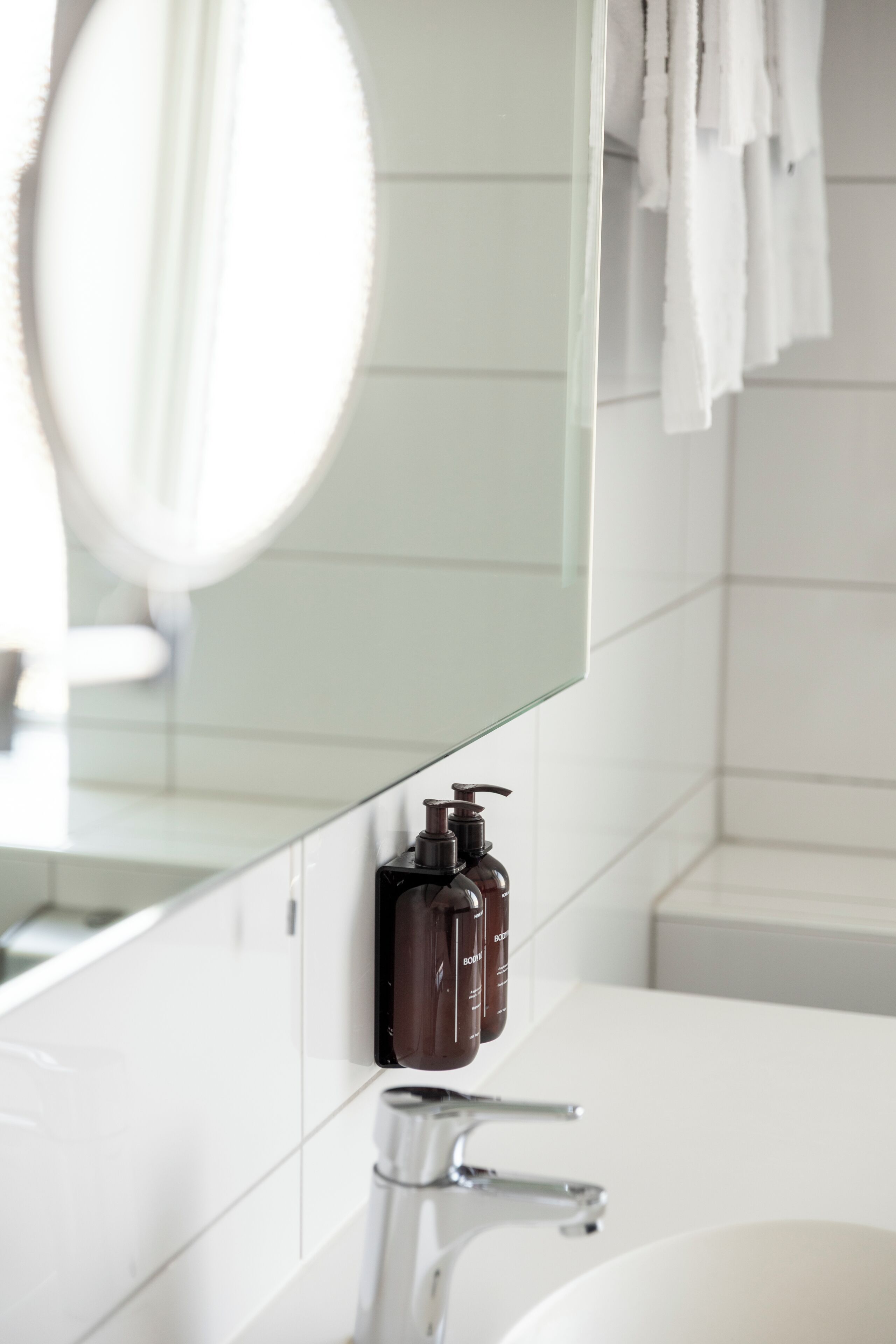 A bathroom with a white sink, a mirror, and a bottle of soap.