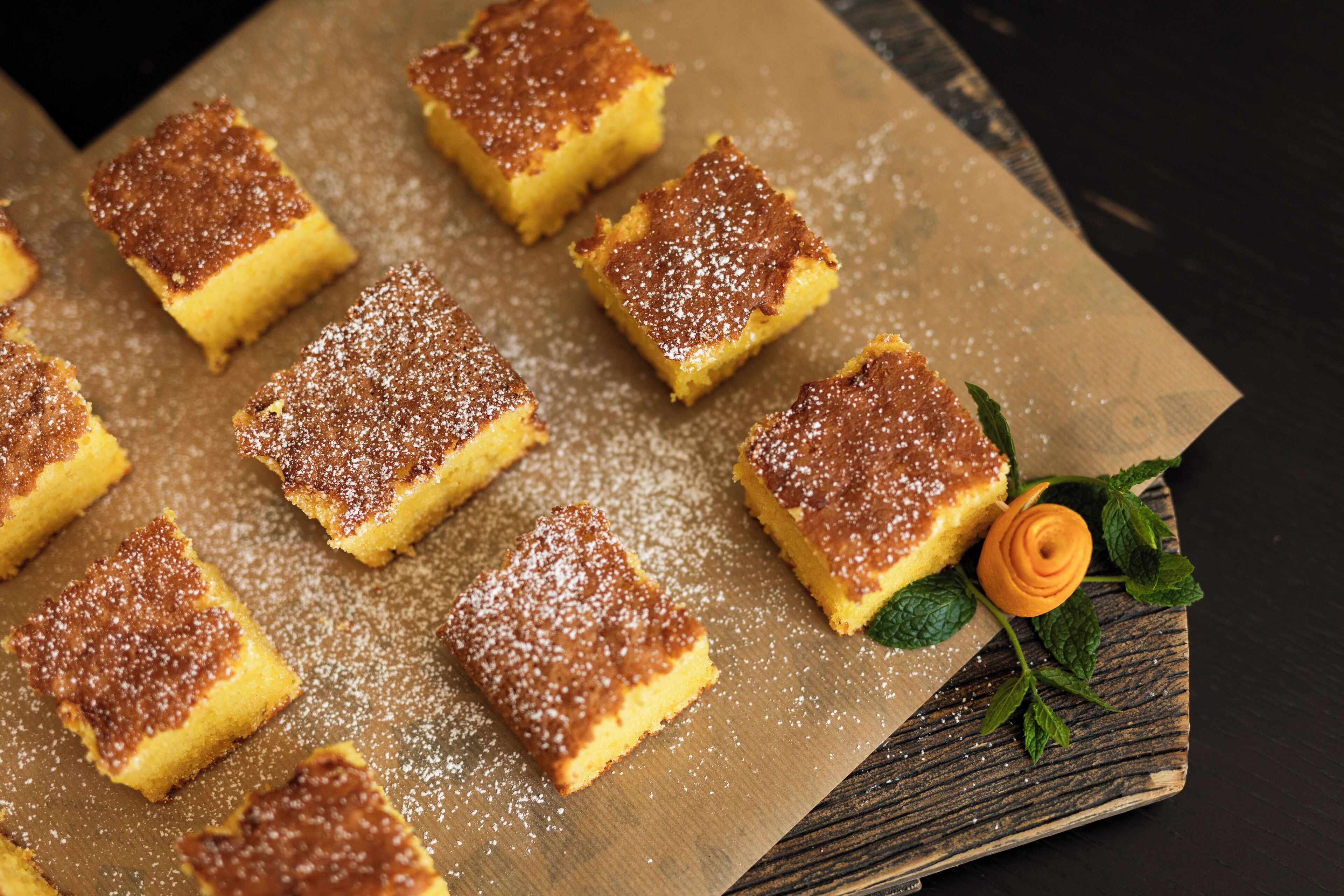 Una bandeja de postres cuadrados espolvoreados con azúcar glass, sobre una superficie de madera.