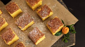 Una bandeja de postres cuadrados espolvoreados con azúcar glass, sobre una superficie de madera.