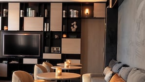 Una sala de estar moderna con un televisor de pantalla plana, mesas redondas con velas y un sofá con cojines.