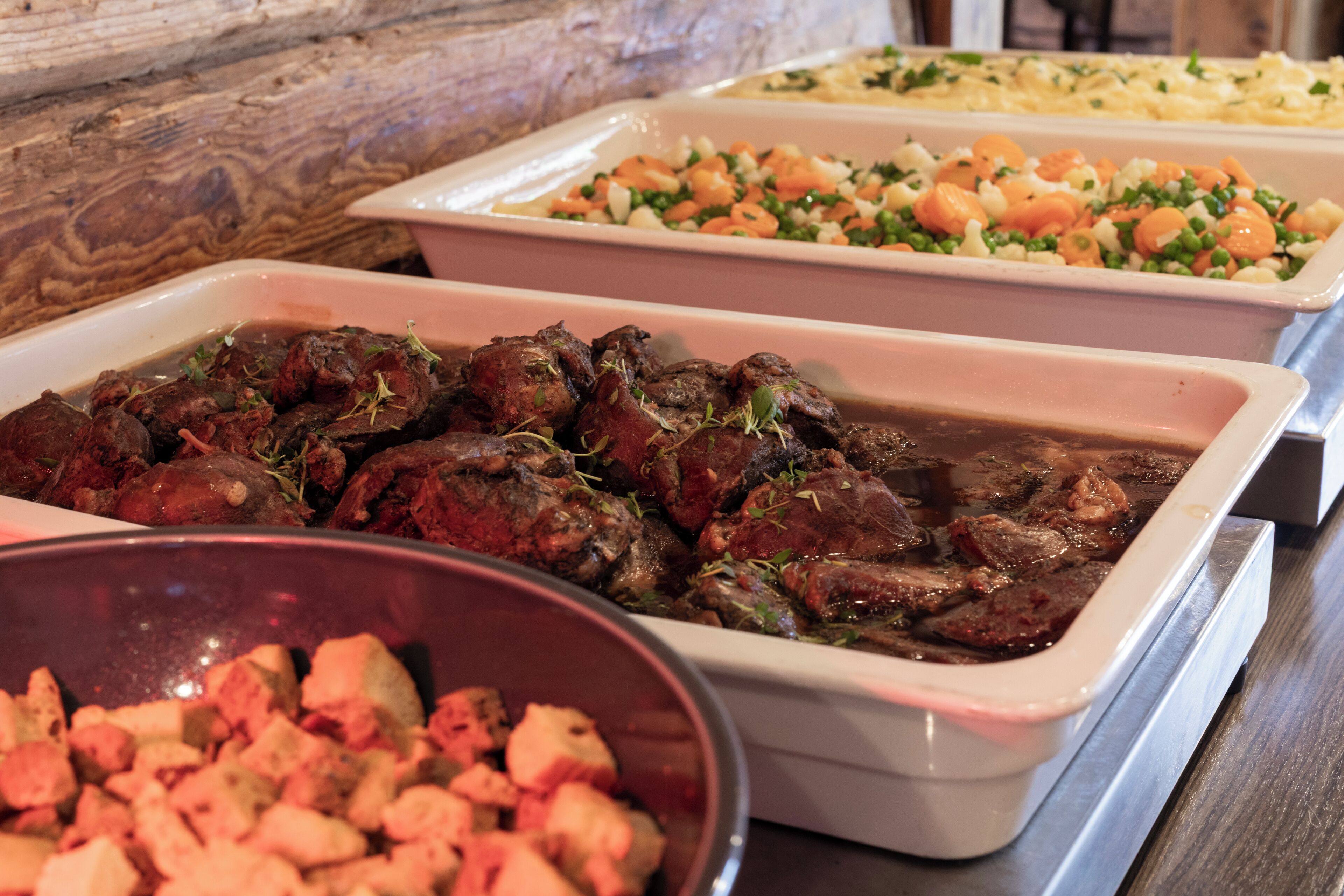 Un buffet con diversi piatti, tra cui carne, verdure e una ciotola di cibo a cubetti.